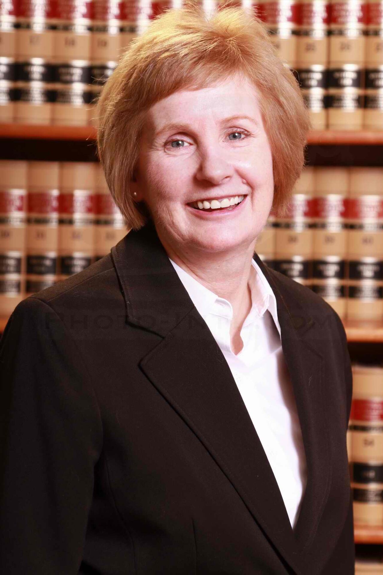 A woman in suit and tie standing next to a book shelf.